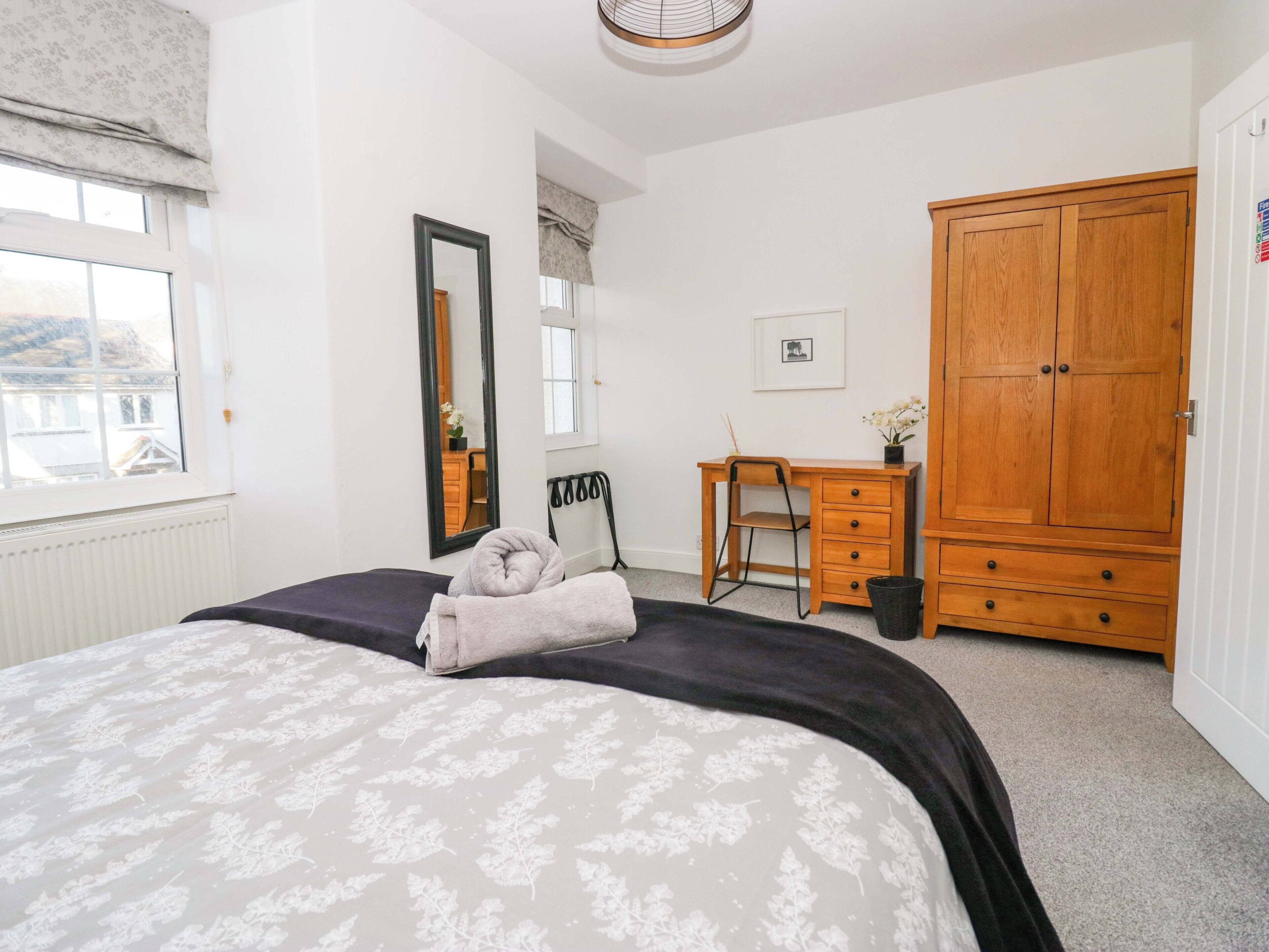 Ein Schlafzimmer mit Bett, Schreibtisch, Kleiderschrank, Spiegel und Fenster.