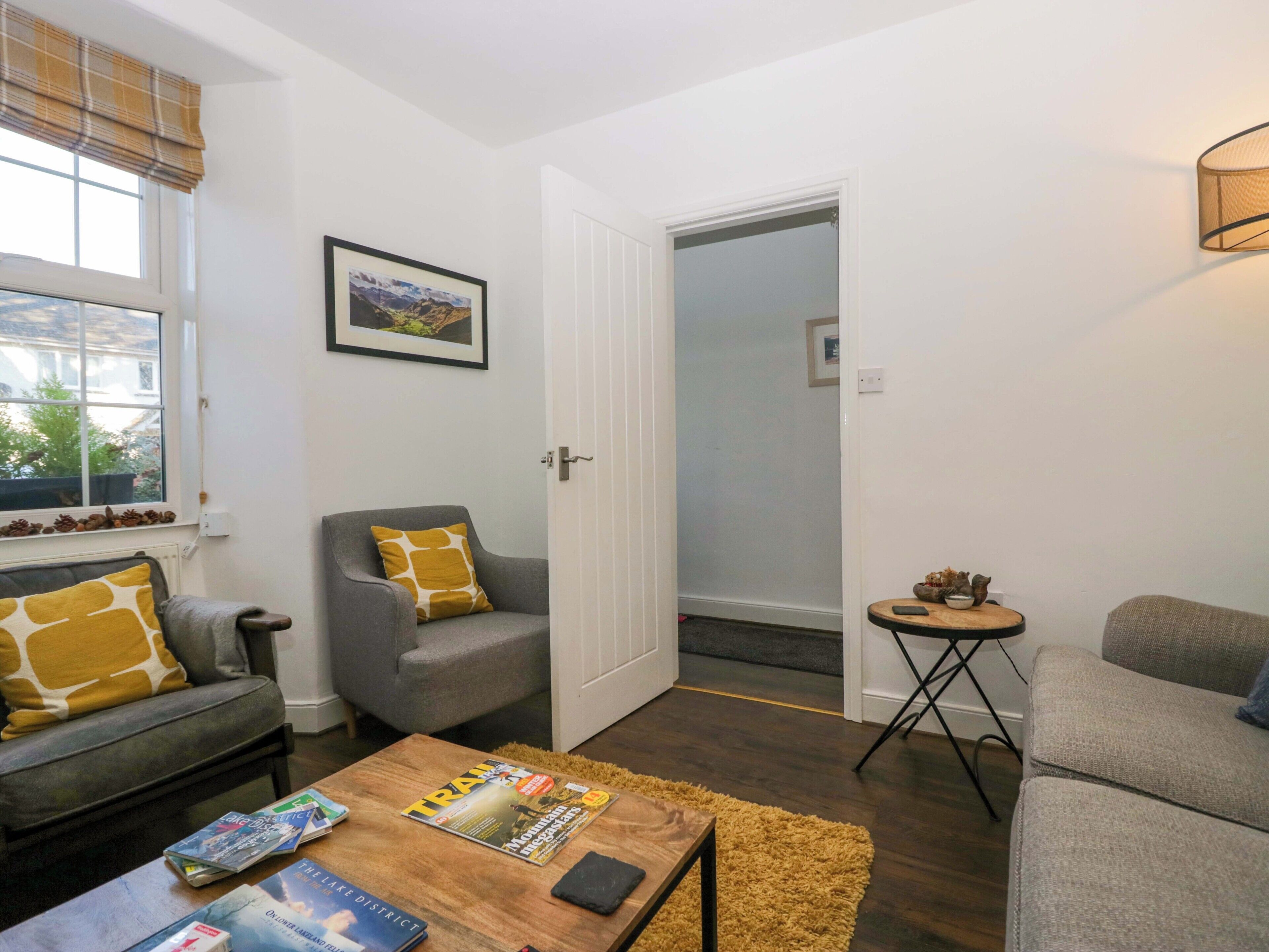 A living room with a sofa, armchair, coffee table, and a small side table. There is a door leading to another room.