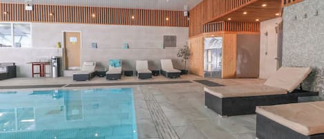 A modern indoor pool area with lounge chairs and a clear pool.