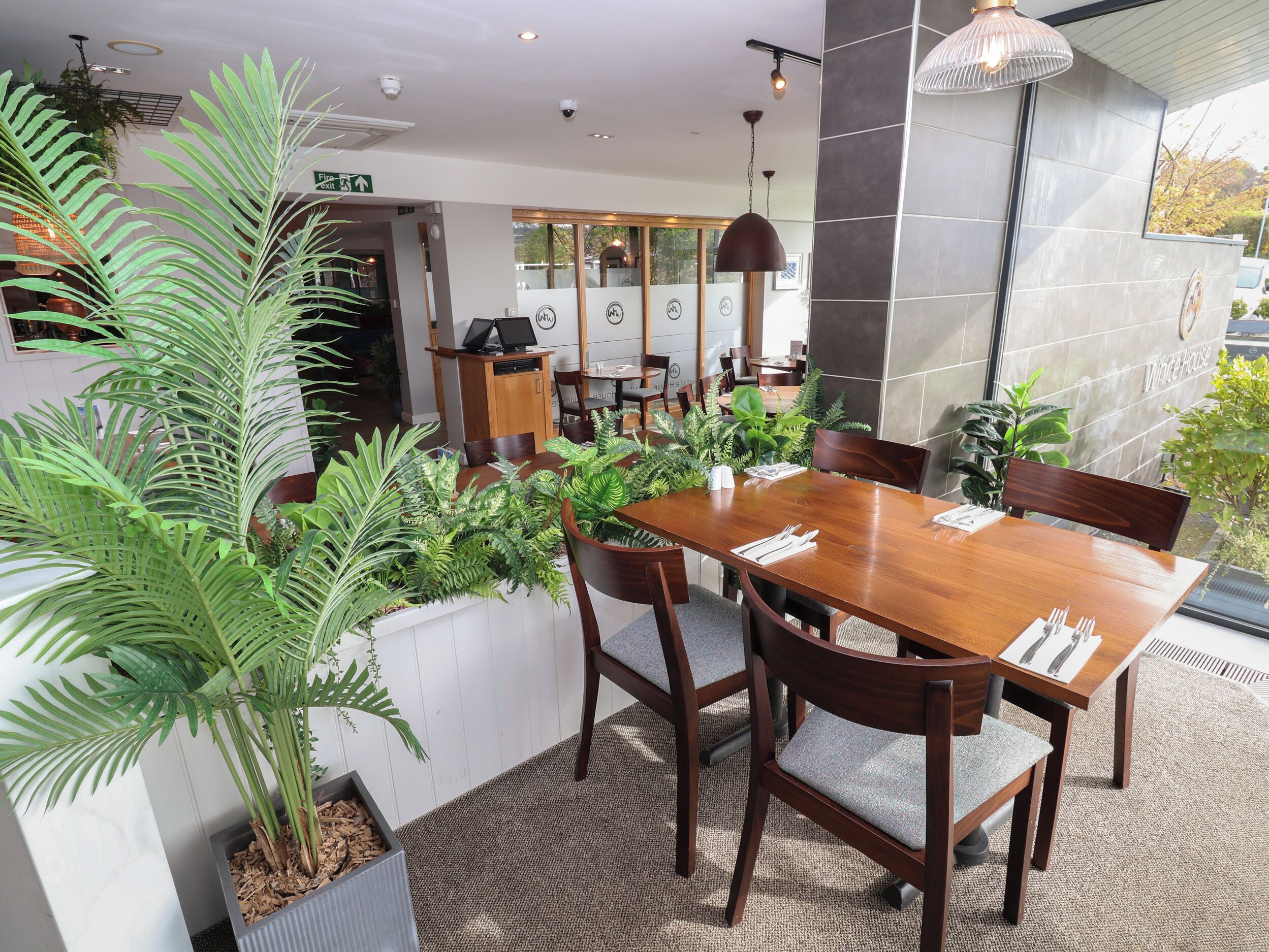 A restaurant with a wooden table and chairs, surrounded by potted plants.
