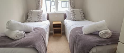 A twin room with two beds, each with a rolled towel, a small wooden nightstand, and patterned pillows.