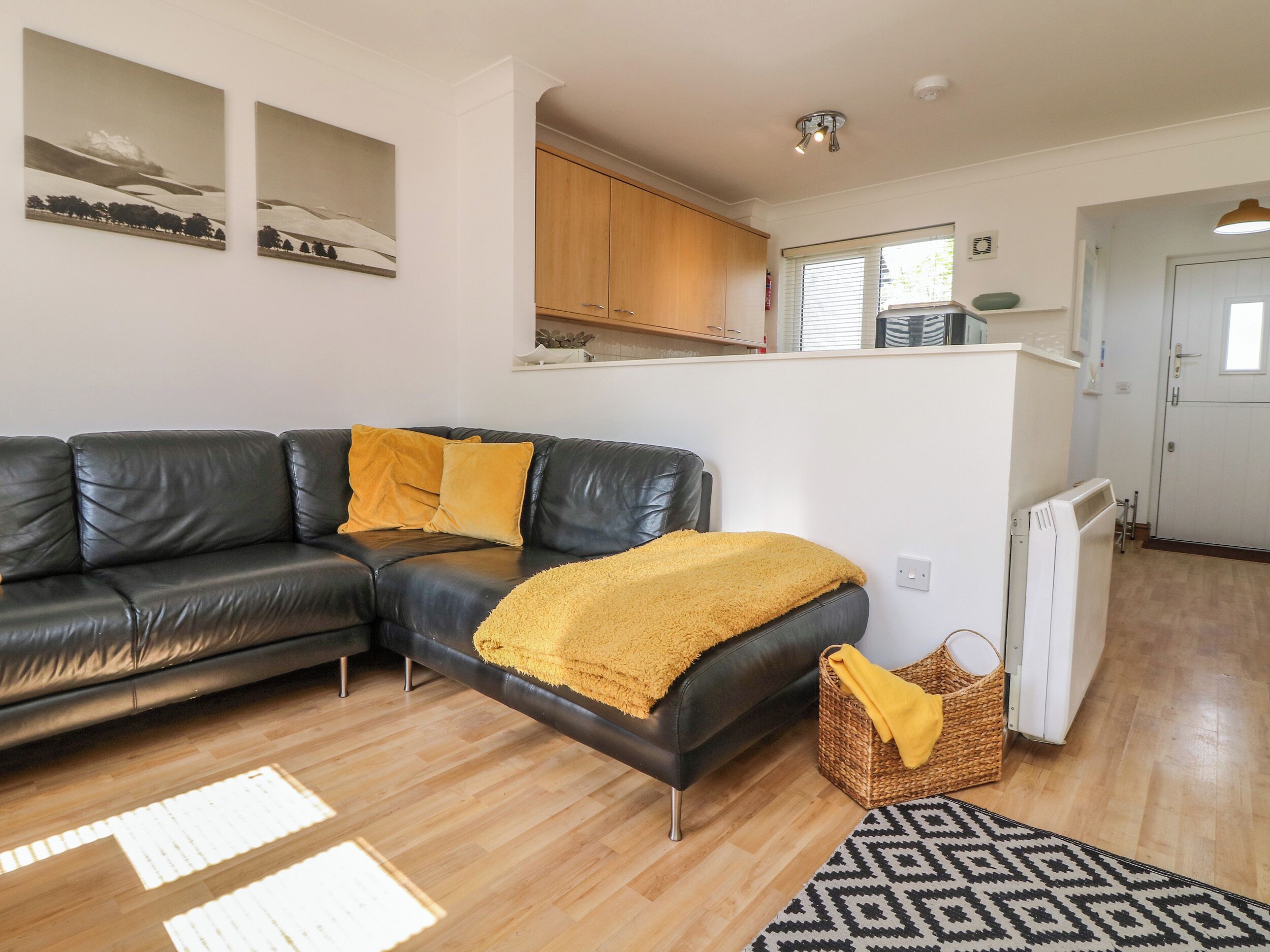 A modern living room with a black leather sofa, a yellow throw blanket, and a patterned rug.