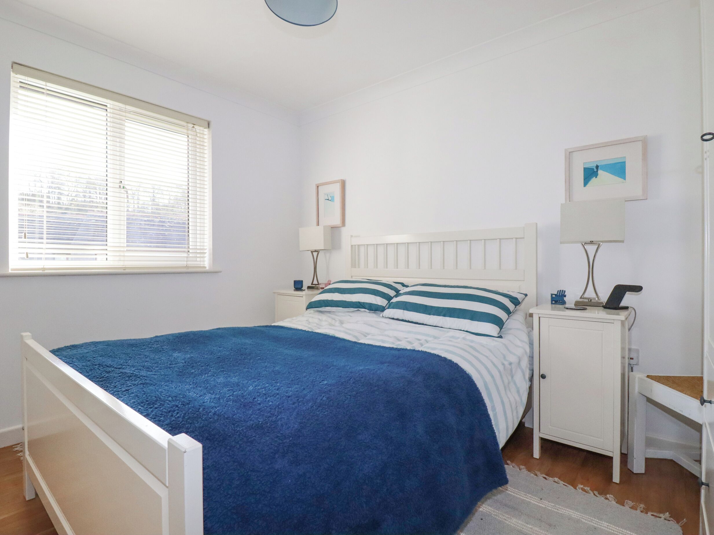 Quarto com cama, mesas de cabeceira, luminária de parede e uma janela com persianas.