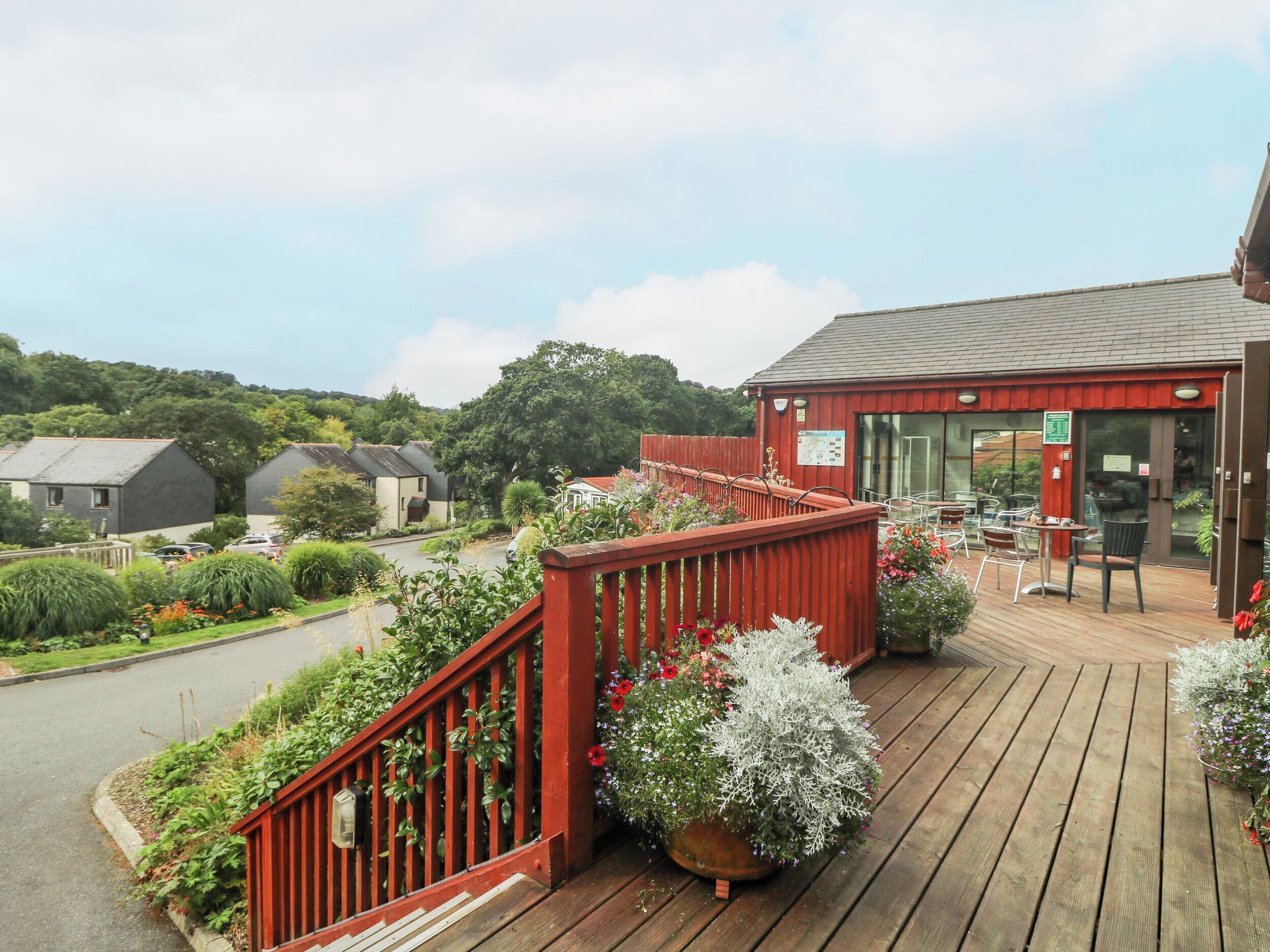 A wooden deck with outdoor seating, surrounded by lush greenery and a red fence.