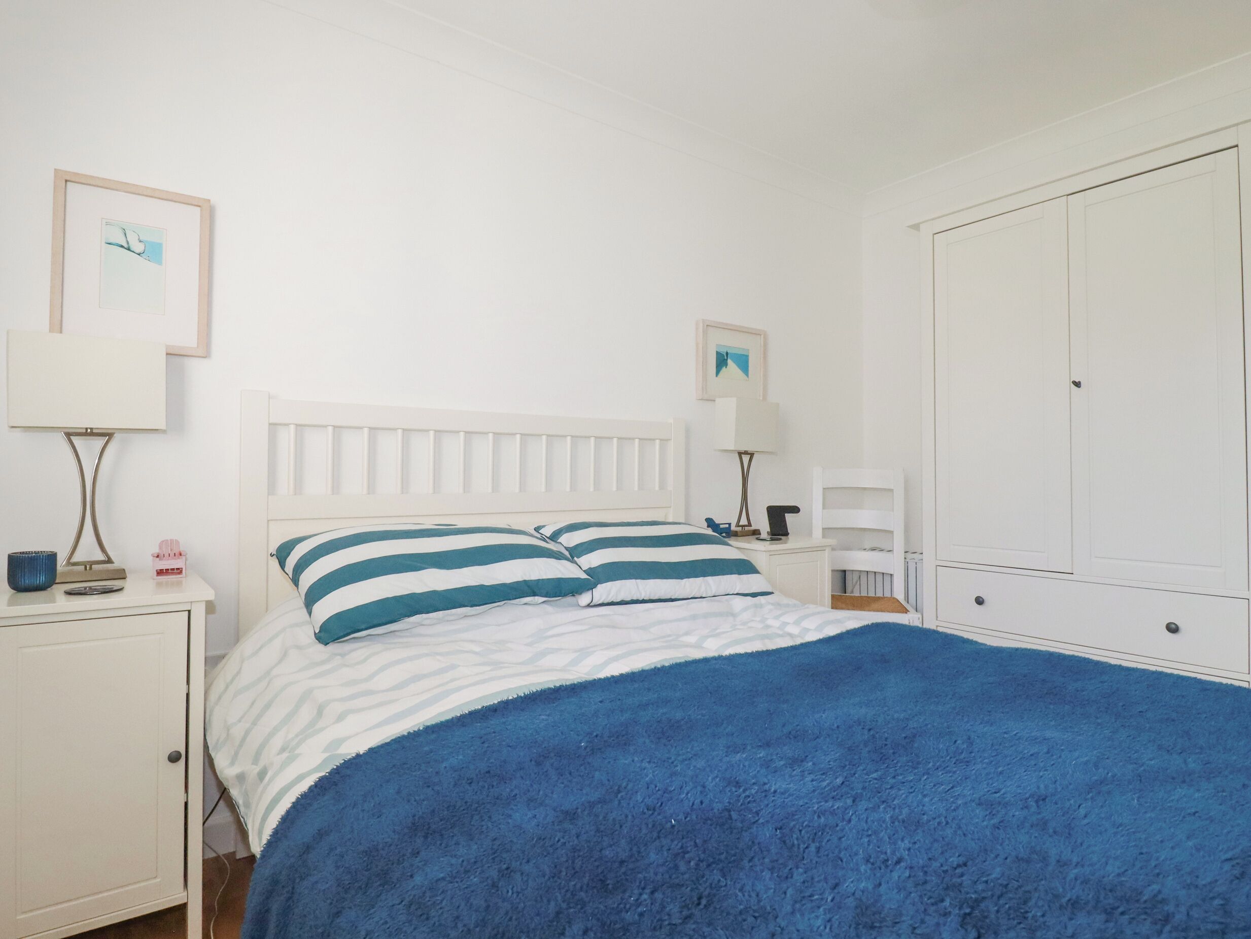 A bedroom with a bed, nightstands, a wardrobe, and two framed pictures on the wall.