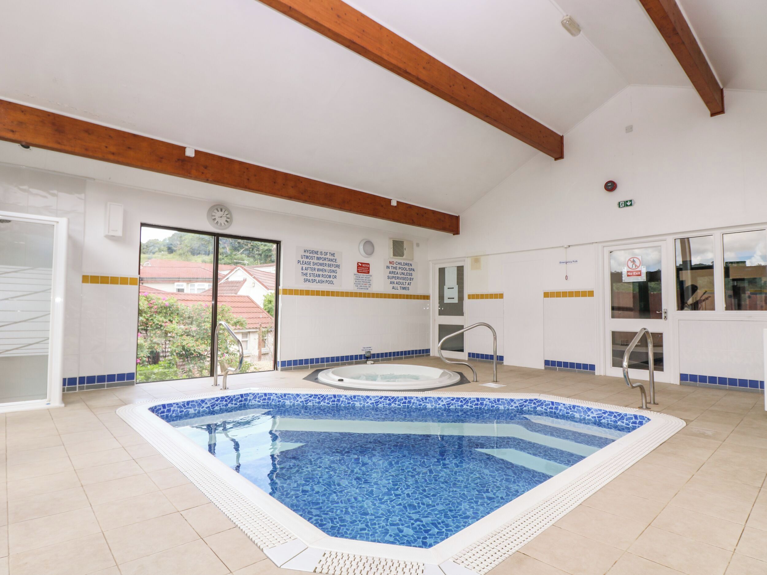 A swimming pool with a tiled edge, a hot tub, and a door with a sign indicating no children allowed in the pool area.