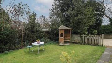 A garden with a wooden playhouse, a round table with chairs, and a potted plant.
