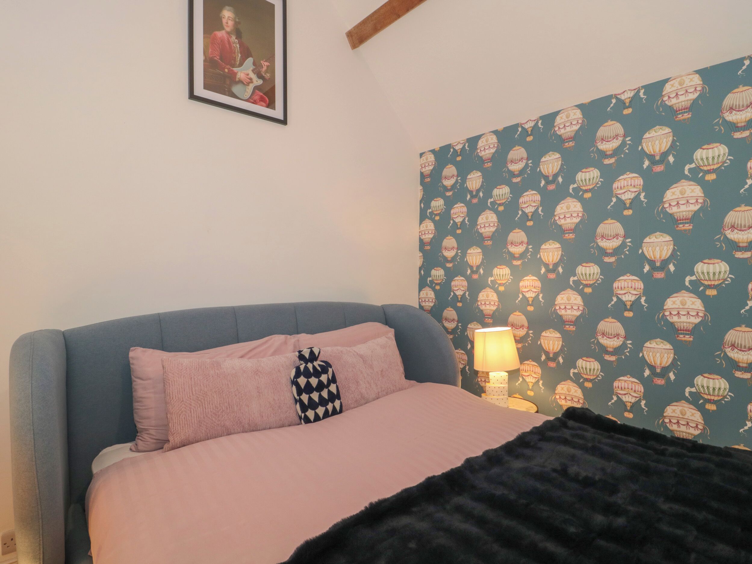 A bedroom with a bed, pillows, a lamp, and a wall with a pattern.