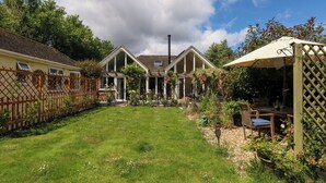 Un grand jardin à l’arrière de la maison, avec une pelouse, une clôture en bois et une pergola agrémentée d’une table et de chaises.