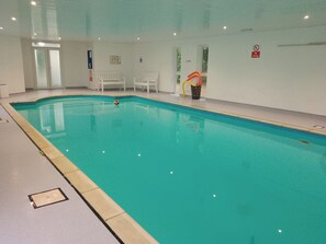 An indoor swimming pool with clear water, white poolside chairs, and a 'No Diving' sign on the wall. - Crystals (Beaworthy)