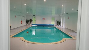 An indoor swimming pool with clear water, a blue lane divider, and safety signs on the walls. - Crystals (Beaworthy)