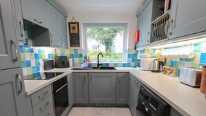 A kitchen with grey cabinets, a black dishwasher, and a window with a view of greenery outside. - Little Hallgarth (Keswick)