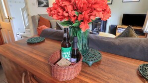 A wooden table with a bottle of beer, a vase with red flowers, and a basket with a coaster and a small item. - Little Hallgarth (Keswick)