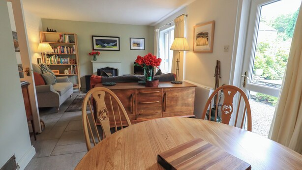 A dining area with a wooden table, chairs, a sofa, a bookshelf, and a fireplace. - Little Hallgarth (Keswick)