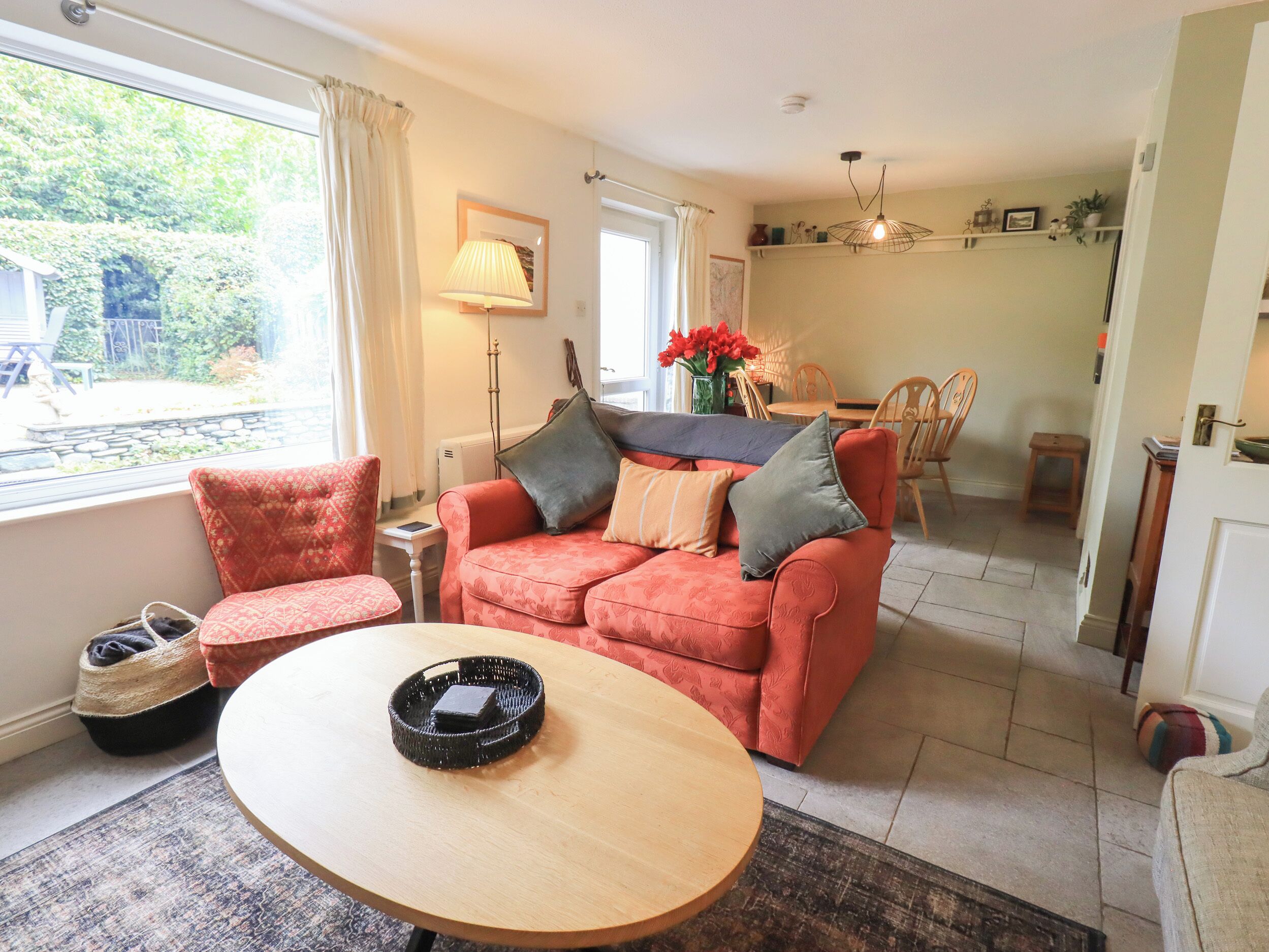 A cozy living room with a red sofa, a round wooden table, and a dining area in the background.