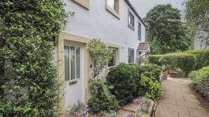 A two-story house with a white exterior, a stone pathway, and potted plants along the front. - Little Hallgarth (Keswick)
