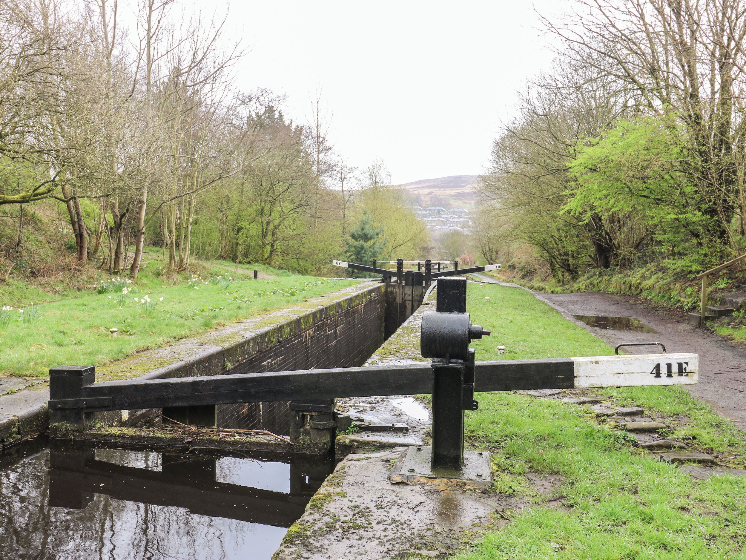 A narrow canal with a lock mechanism, surrounded by grassy banks and trees.