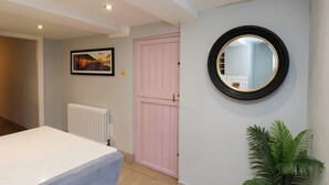 A room with a bed, a radiator, a pink door, a round mirror, and a potted plant. - Kitty's Cottage (Whitby)
