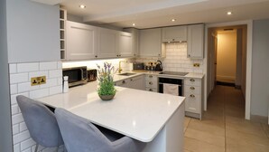 A modern kitchen with white cabinets, a central island, a microwave, and a sink. - Kitty's Cottage (Whitby)
