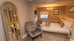 A bedroom with a bed, a chair, a mirror, a radiator, and a window. - Kitty's Cottage (Whitby)