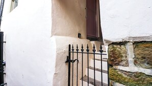 A white building with a stone base, a black metal gate, and a brown door. - Kitty's Cottage (Whitby)