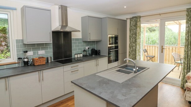 A modern kitchen with grey cabinets, a stainless steel range hood, and a built-in oven. - Hedgehogs Cottage (Glenrothes)