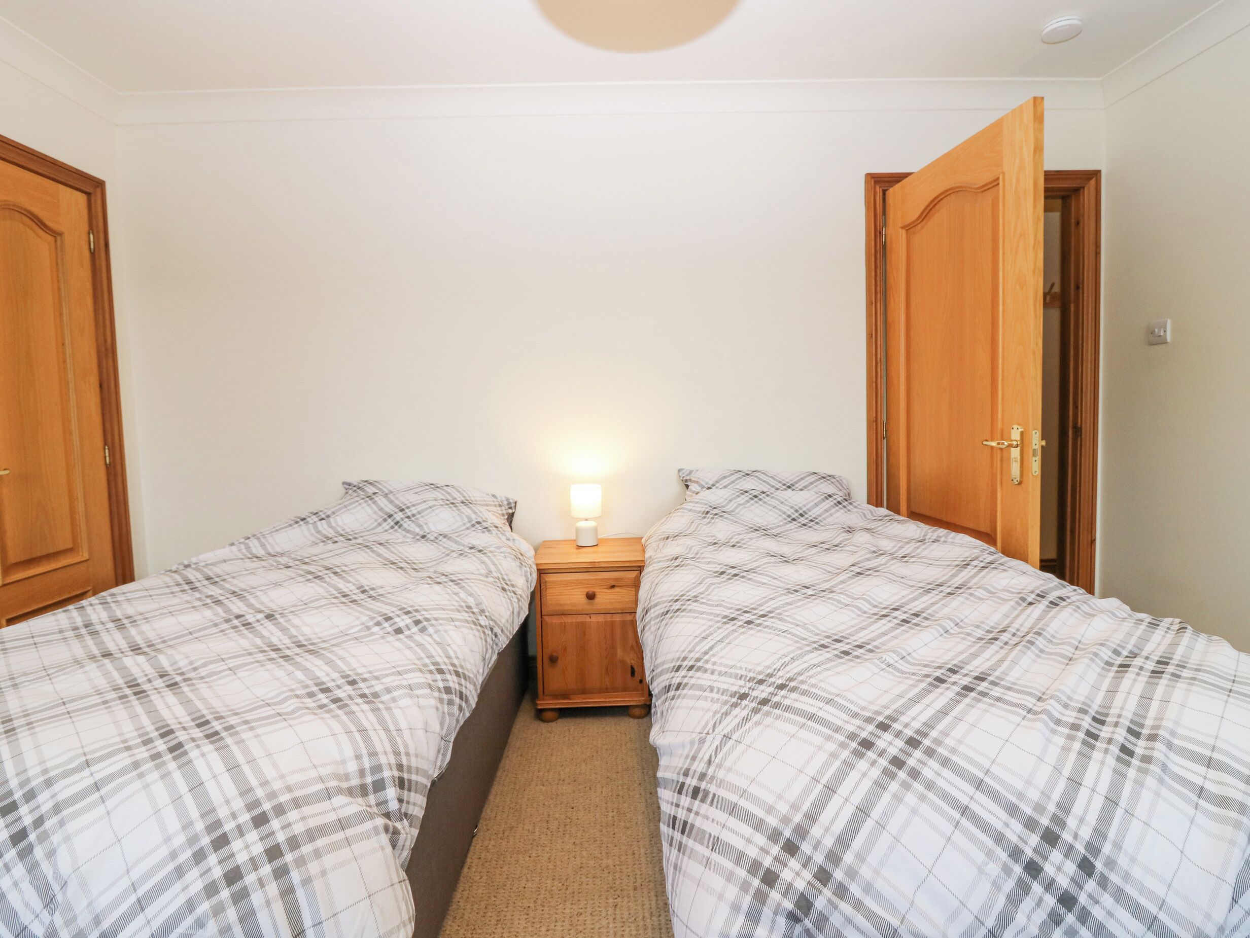 A bedroom with two beds, a nightstand with a lamp, and wooden doors.