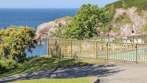 A pool area with a wooden fence, chairs, and a view of the sea. - Ocean View (Ilfracombe)