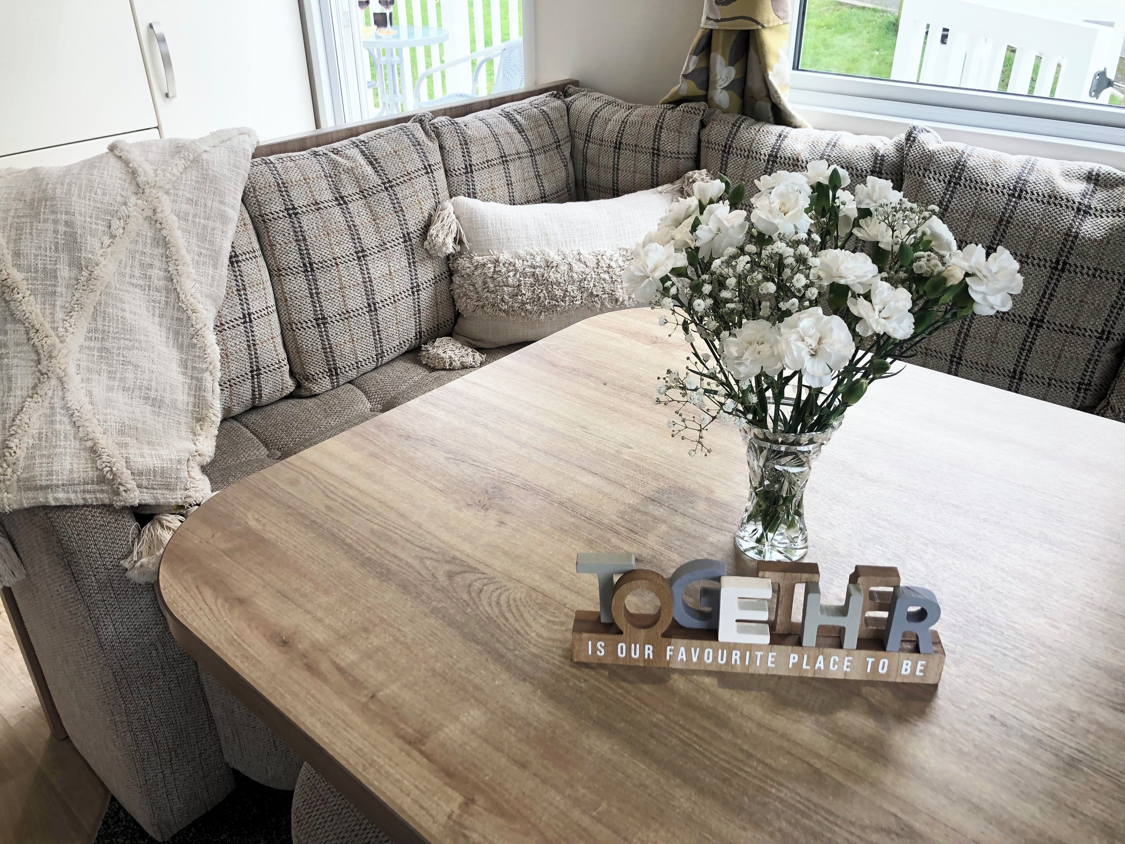 A cozy seating area with a wooden table, a vase of white flowers, and a sign that reads "TOGETHER IS OUR FAVOURITE PLACE TO BE".