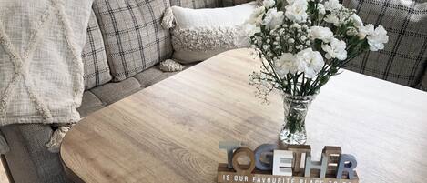 A cozy seating area with a wooden table, a vase of white flowers, and a sign that reads "TOGETHER IS OUR FAVOURITE PLACE TO BE".