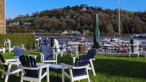 A marina with boats, a grassy area with Adirondack chairs, and a hill with houses in the background.