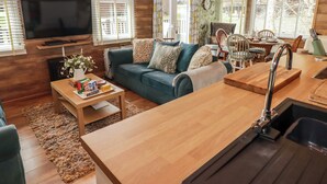 Ein modernes Wohnzimmer mit Holzboden, einem blauen Sofa, einem Couchtisch, einem Fernseher und einer Küchenzeile mit Spüle und Holz Arbeitsplatte.
