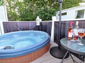 A hot tub with a wooden surround, a glass table with wine glasses and bottles, and a lantern on a post. - 25 Kingfisher Court (Lincoln)