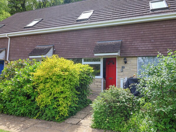 Une maison à deux étages avec une porte rouge, un petit jardin et le numéro « 50 » bien visible sur le mur.