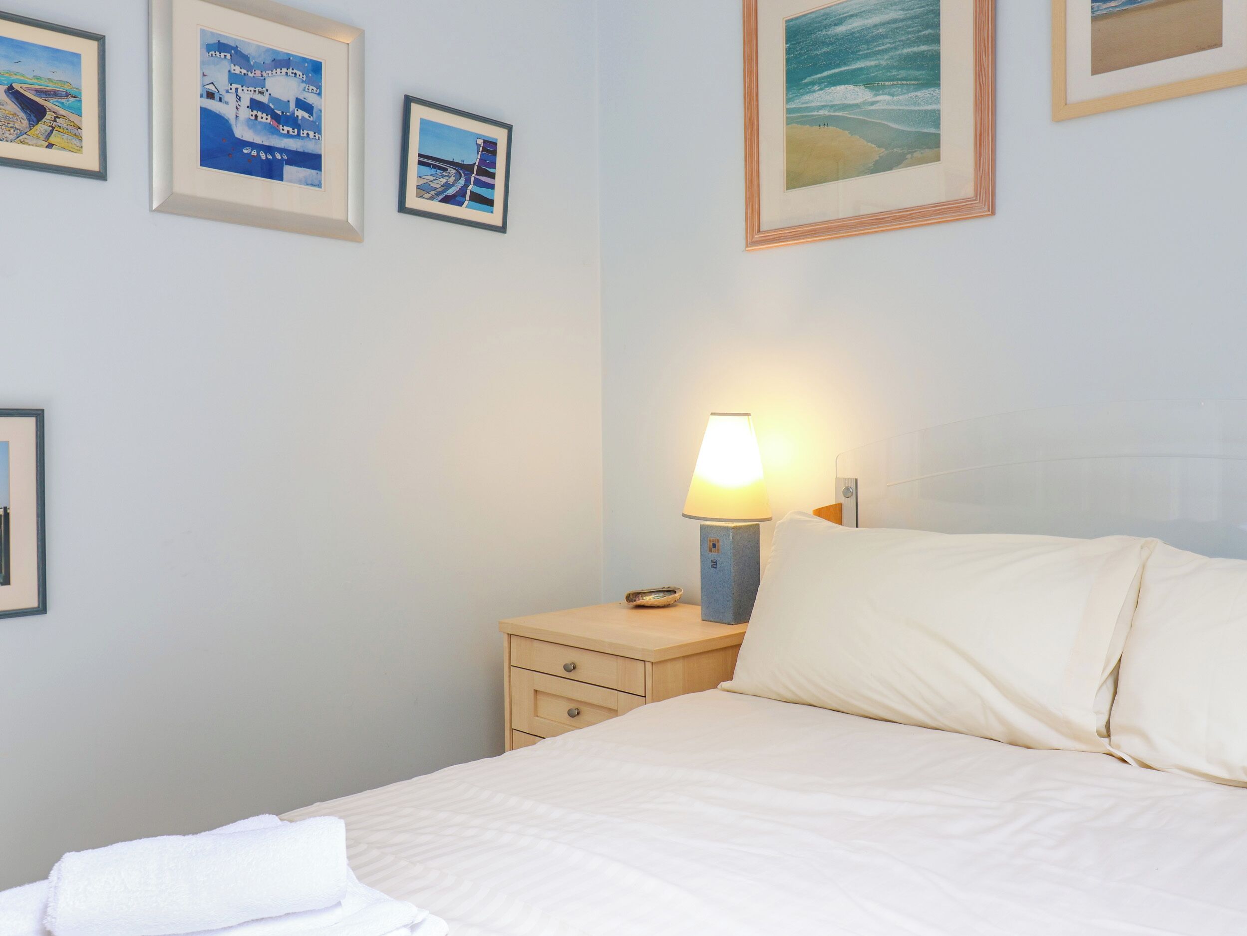 A hotel room with a bed, a nightstand with a lamp, and framed pictures on the wall.