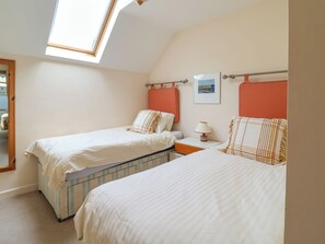 Une chambre avec deux lits, une lucarne, une table de chevet avec une lampe et un tableau encadré au mur.