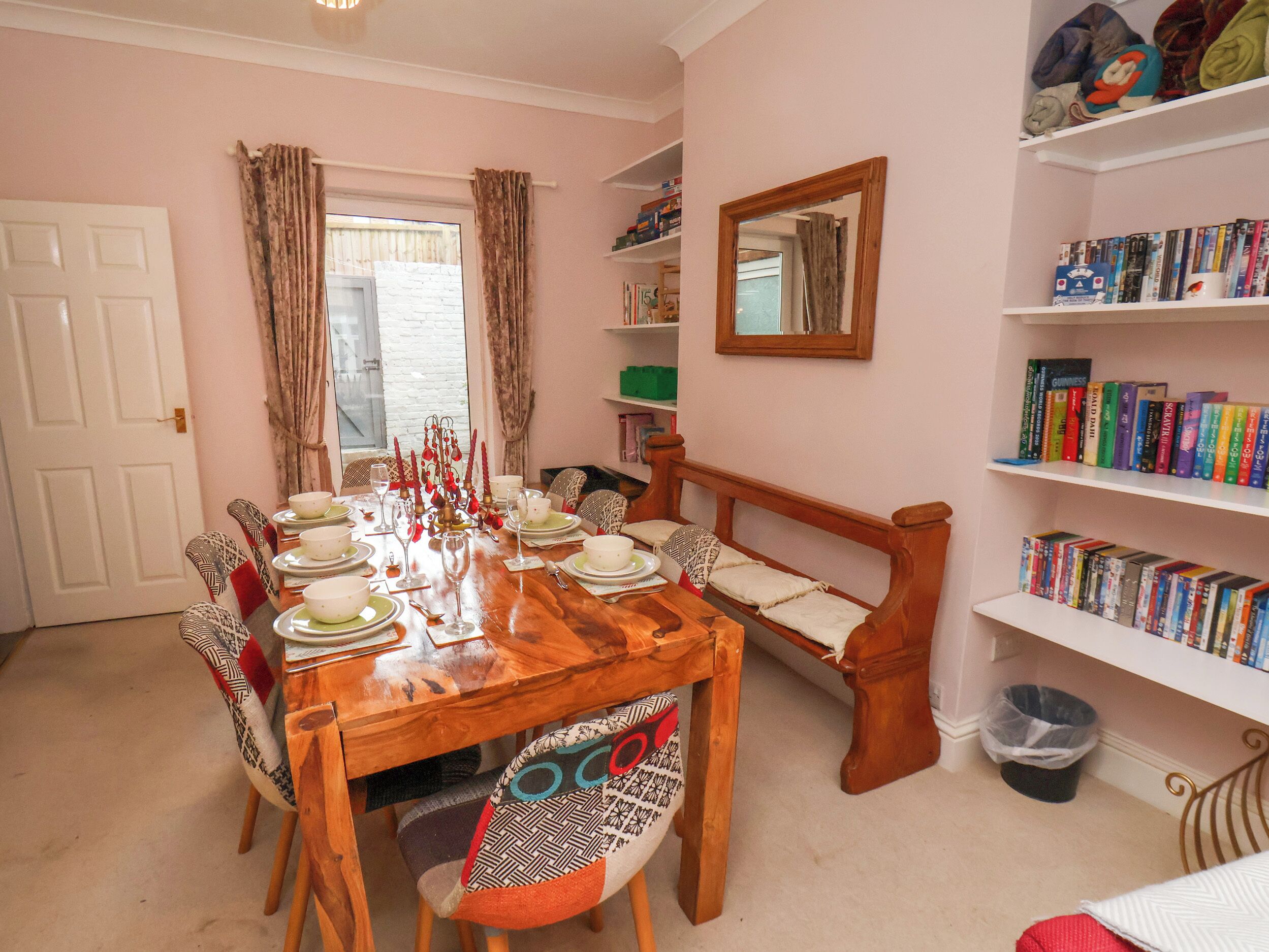 A dining room with a wooden table set for six, a bench, and a bookshelf filled with books.