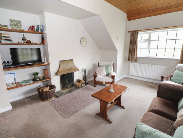 A cozy living room with a fireplace, a television on a shelf, a clock on the wall, and a window with curtains. - Ben Brack (Oughterard)