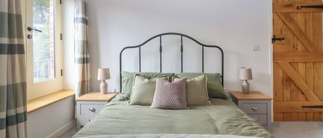 A bed with a metal frame, two bedside tables, a window with curtains, and a wooden door.