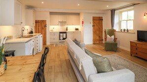 A modern kitchen with white cabinets, a wooden dining table, and a sofa in the living area. - 8 Rookhaye (Salisbury)