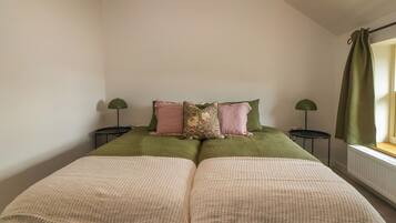 A bedroom with a bed, two bedside tables, a window with curtains, and a radiator.