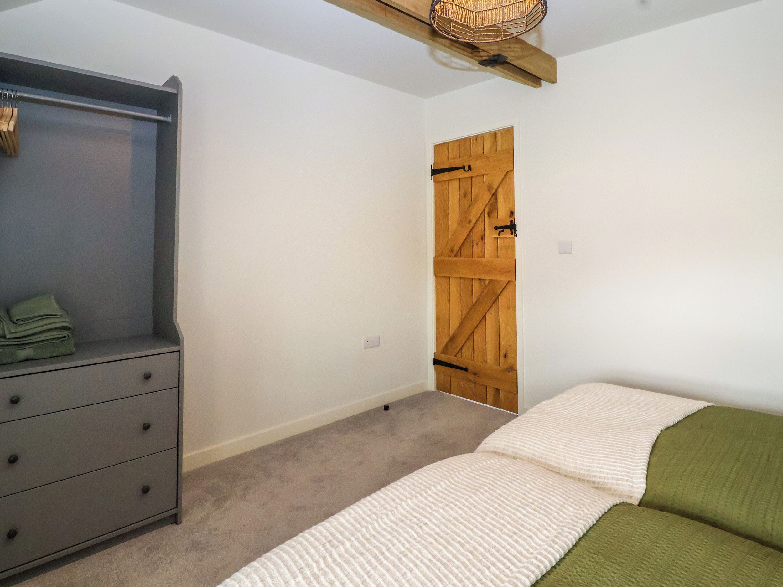 A bedroom with a grey dresser, a wooden door, and a bed with green and white bedding.