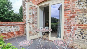 A patio with a table and two chairs, a door leading to a covered area, and a brick wall. - 8 Rookhaye (Salisbury)
