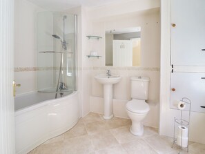 Kylpyhuone, jossa on lasiseinällä varustettu suihku, jalkojen alla oleva allas ja wc.
