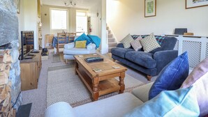 A cozy living room with a fireplace, a dining area, and a staircase leading to another level. - Glasfryn (Dolgellau)