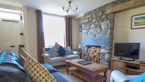 A cozy living room with a stone fireplace, a television, and a sofa with patterned cushions. - Glasfryn (Dolgellau)