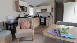 A compact living space with a kitchenette, a sofa, a dining table, and a chair. - Tri-star House (Bridport)