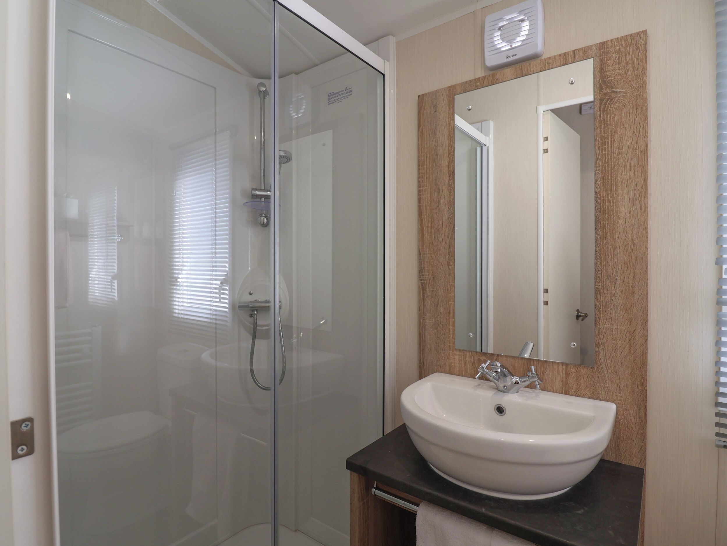 Une salle de bain moderne avec une douche à parois de verre, un lavabo blanc et un miroir avec un cadre en bois.