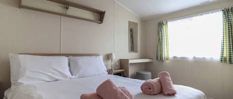 A hotel room with a large bed, a bedside table, a mirror, and a window with curtains.
