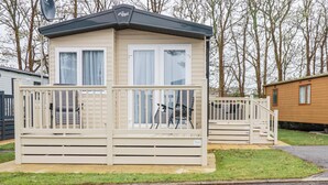 Ein kleines, eingeschossiges Mobilheim mit Balkon und überdachter Veranda.